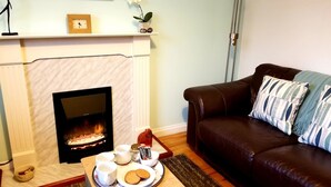 A cozy living room with a fireplace, a brown leather sofa, and a tray with cookies and cups. - Dunshee (Dunvegan)
