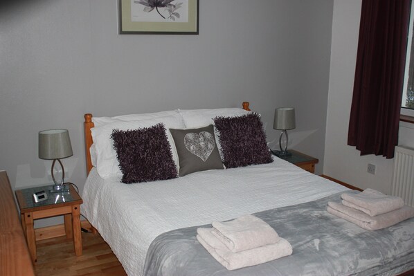 A neatly made bed with white bedding and decorative pillows, a bedside table with a lamp, and a framed picture on the wall.