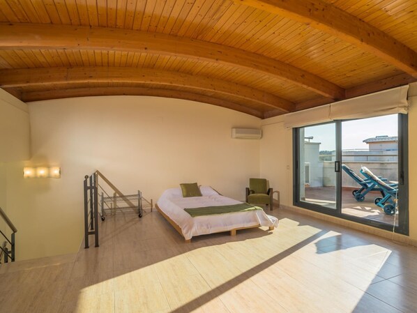 A bedroom with a bed, a chair, a staircase, and a balcony with sun loungers.