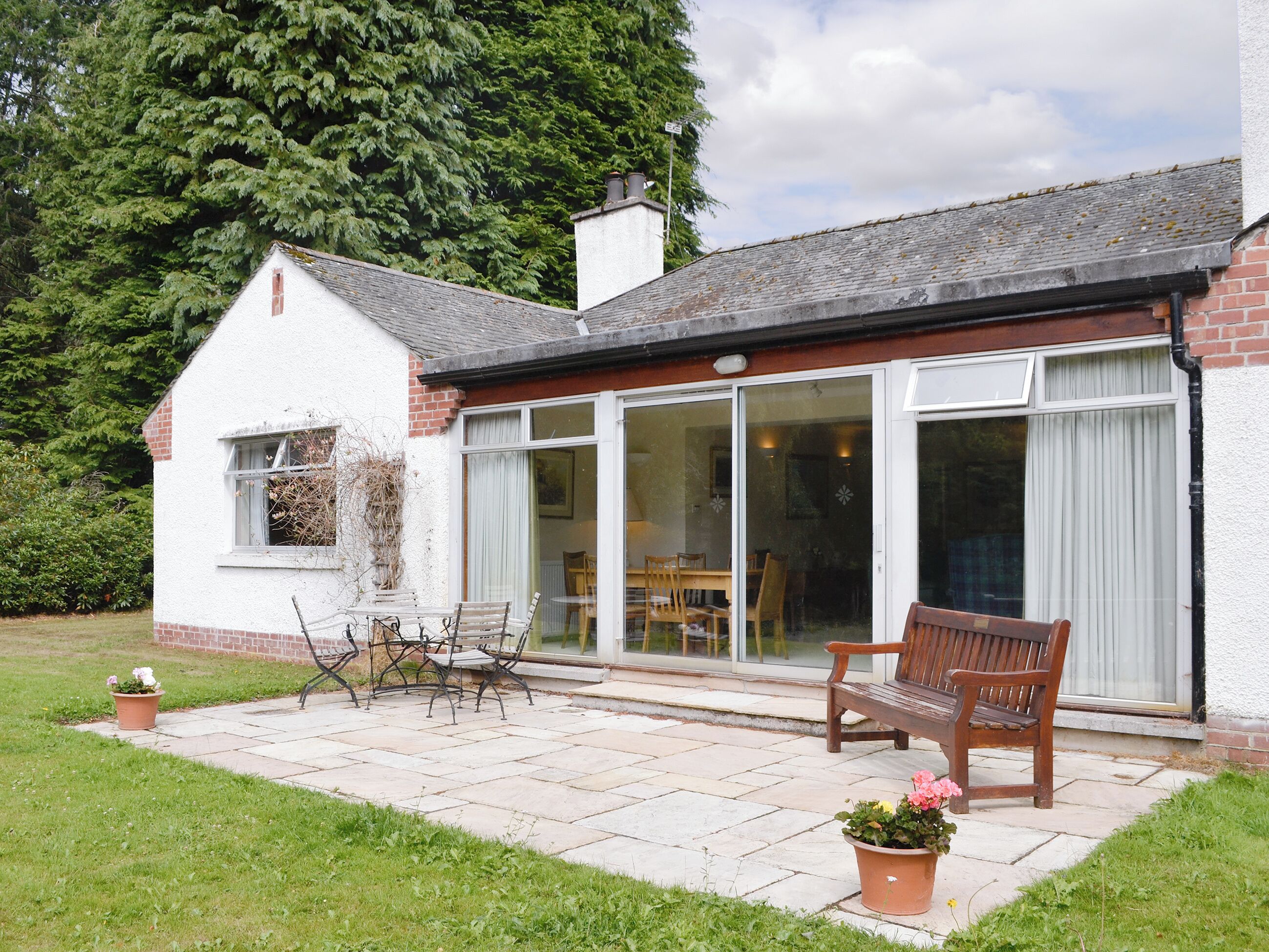 A house with a patio, a wooden bench, and a table with chairs.