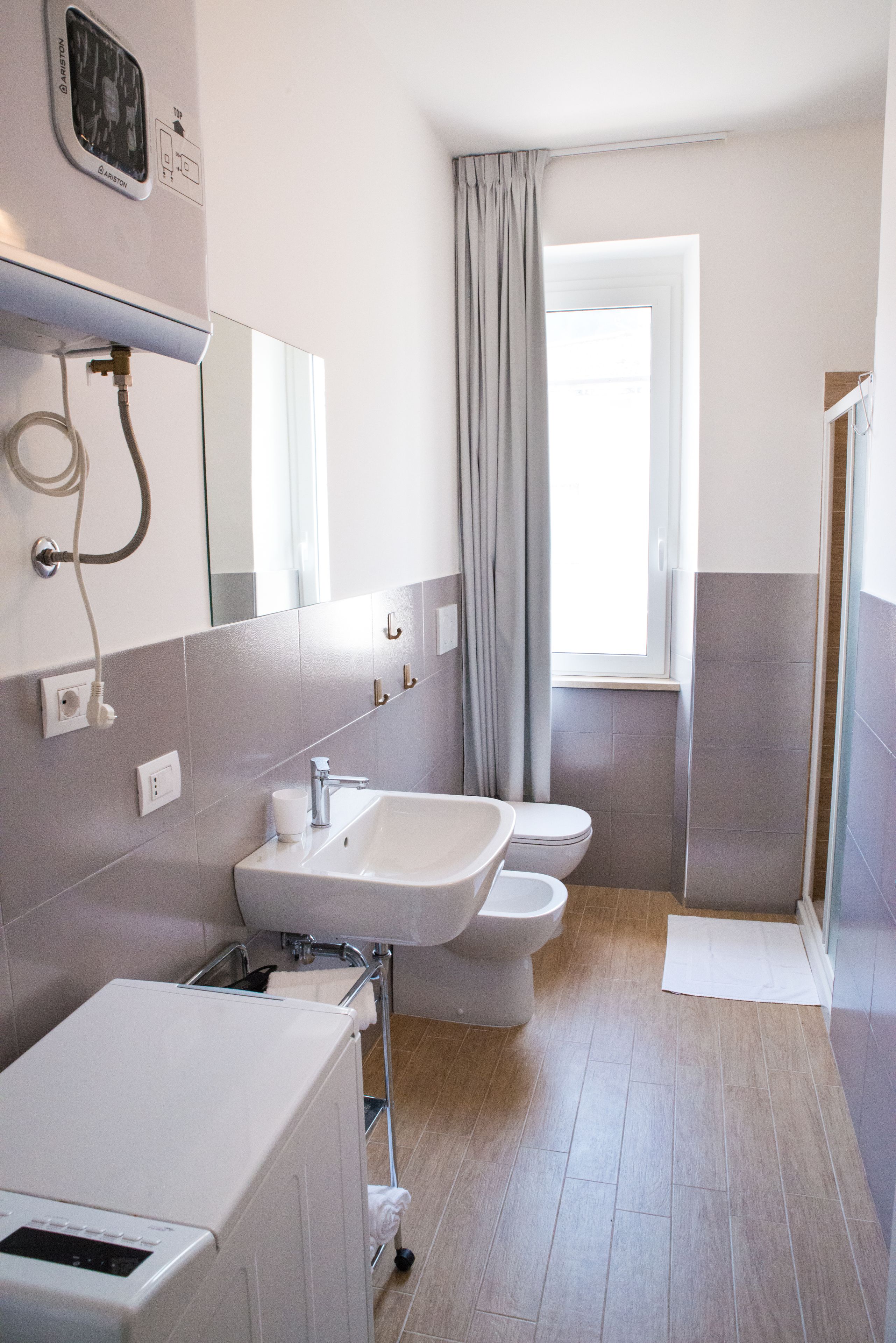 A modern bathroom with a sink, toilet, and shower. There is a window with curtains, a towel rack, and a mirror above the sink.