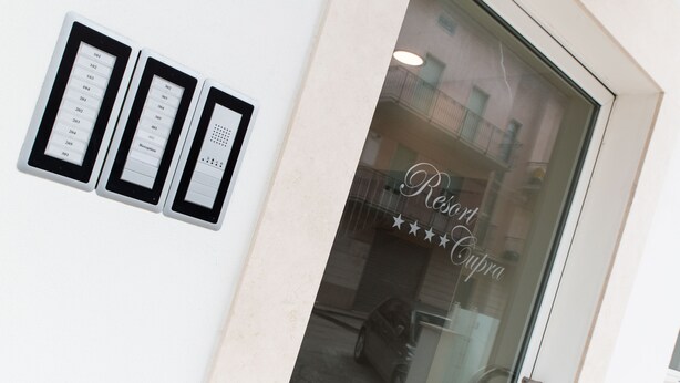 A reception desk with a glass door, a sign reading "Resort Cupra", and a wall-mounted directory with room numbers. - Resort Cupra (Cupra Marittima)