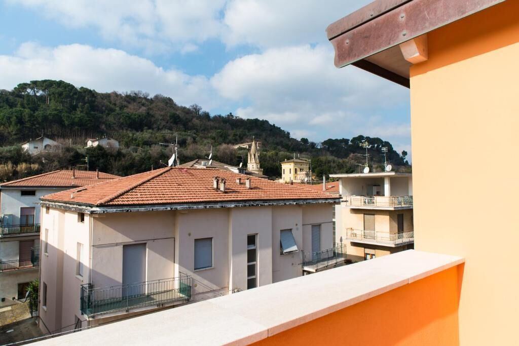 Un edificio residencial con techo de tejas rojas, un balcón y vistas a una colina con árboles.