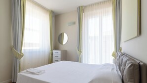 A hotel room with a large bed, a bedside table, a mirror, and curtains. - Resort Cupra (Cupra Marittima)
