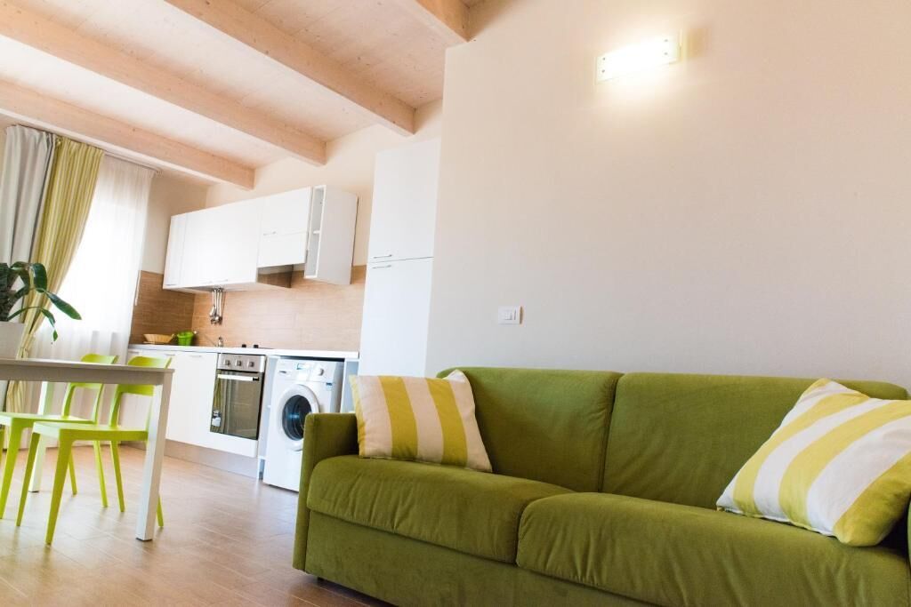 Een moderne keuken met witte kasten, een wasmachine en een eethoek met een groene tafel en stoelen.