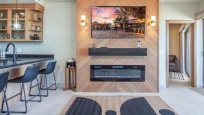 A modern kitchen with a wooden herringbone wall, a large flat-screen TV, built-in bar, and a sleek black countertop.