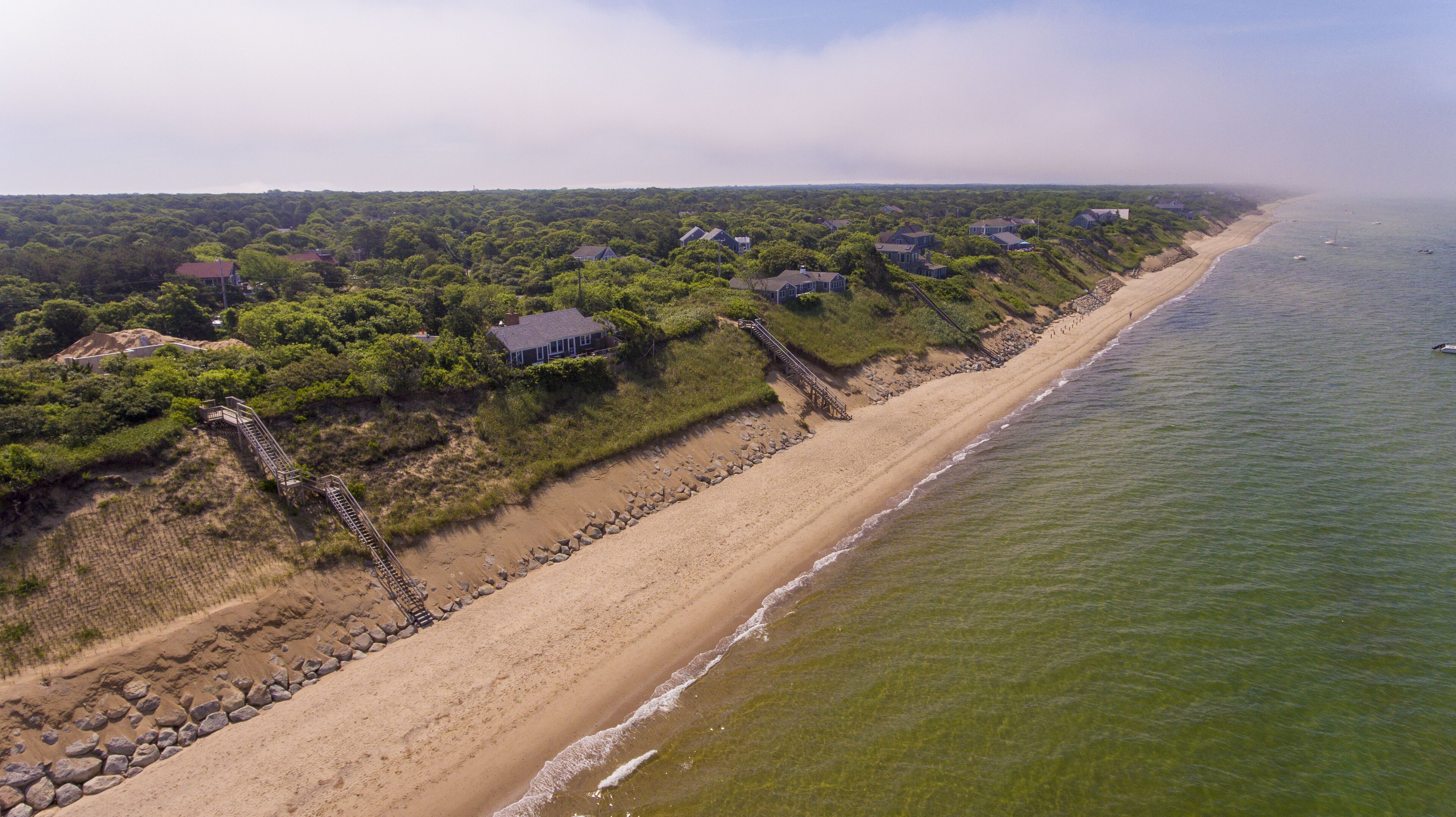 A coastal property with a sandy beach, a wooden staircase leading to a house, and a view of the ocean.