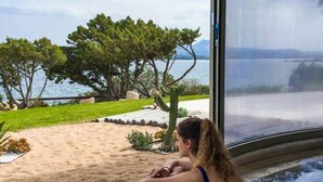 A person relaxing in a hot tub with a view of a lake and trees. - Holiday House - 5 people, 22 m² living space, 2 bedroom, Internet/WIFI, Internet access (Cannigione di Arzachena)