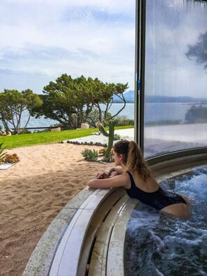 A person relaxing in a hot tub with a view of a lake and trees. - Holiday House - 5 people, 22 m² living space, 2 bedroom, Internet/WIFI, Internet access (Cannigione di Arzachena)