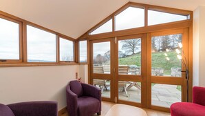 Una habitación con ventanas amplias, piso de madera y dos sillones morados.
