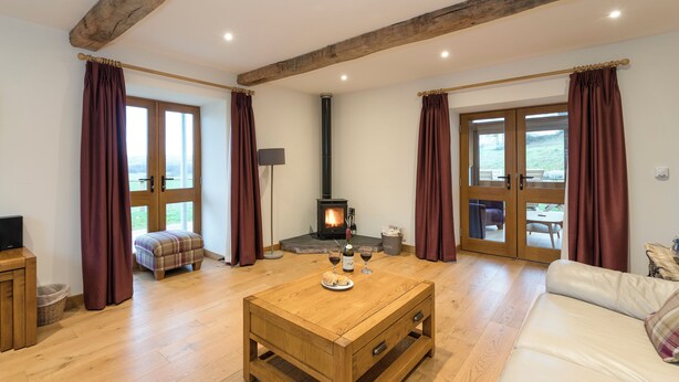 Una habitación acogedora con suelo de madera, un sofá, una mesa de centro, una chimenea y ventanas grandes.