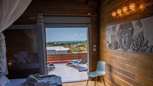 A bedroom with a large sliding glass door leading to a balcony with a view of the ocean.