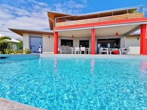 Una casa moderna con piscina, area salotto esterna e terrazza in legno.