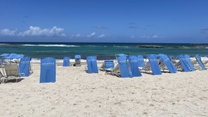 A beach with rows of blue beach chairs labeled "Atlantis" and a rocky shoreline in the background. - 3 Bedroom Lockoff  Harborside Atlantis April 19-26, 2025 with 10 Wristbands (Nassau)