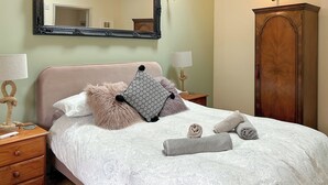 A neatly made bed with a patterned bedspread, two pillows, and rolled towels.