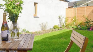 A wooden table with a bottle and glasses, a white building, a wooden fence, and a grassy yard.