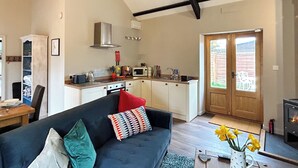 A living room with a dark sofa, a kitchen with white cabinets, a microwave, and a fireplace.