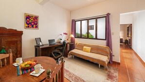 Una sala de estar acogedora con una mesa de comedor de madera, un sofá, un escritorio con una computadora portátil y un amplio ventanal con cortinas.