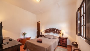 Un dormitorio con cama, mesitas de noche, televisor y ventana.