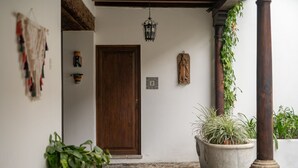 Una entrada empedrada con puerta de madera, plantas en macetas y un farol colgante.