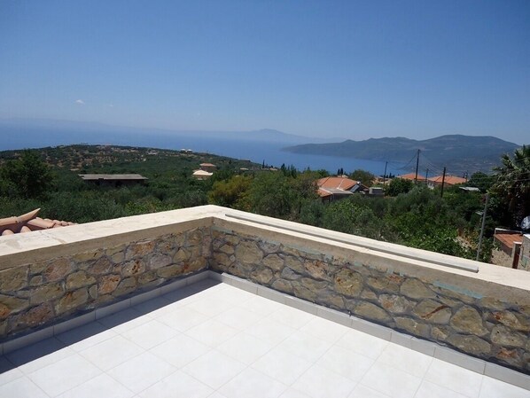 A rooftop terrace with a stone wall and a view of a coastal landscape.