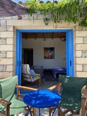 Une pièce avec une porte bleue, deux chaises vertes, une table bleue et un tableau accroché au mur.