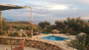 Area piscina con pareti in pietra e una pergola, immersa in un paesaggio naturale e nella vegetazione.