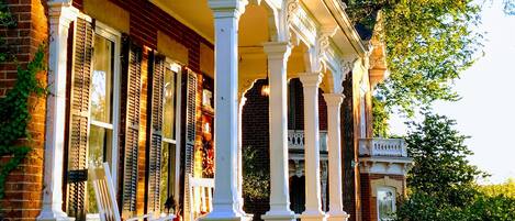 A brick house with a white porch and columns, surrounded by trees and pumpkins.