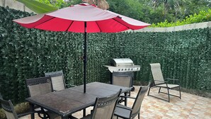 An outdoor patio with a table and chairs, a grill, and a red umbrella. - Three bedroom apartment with private pool (Sosua)