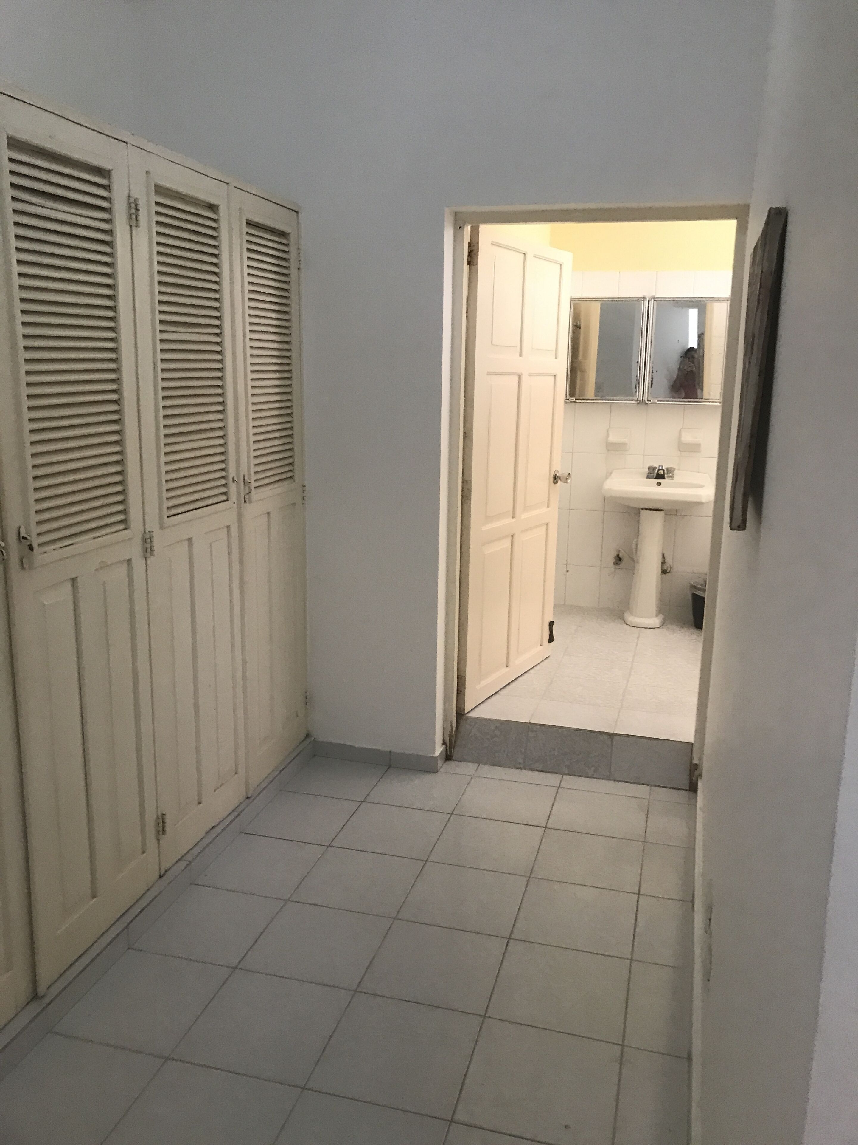 A narrow hallway with a tiled floor leading to a bathroom with a sink and mirror.