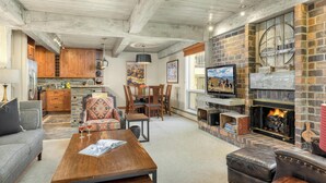 Amplia sala de estar con chimenea, muebles de madera y una cocina al fondo.
