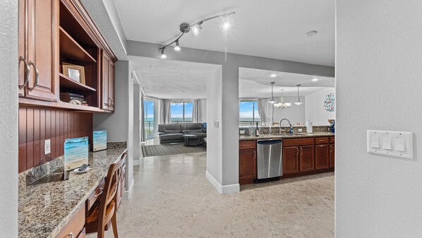 A spacious kitchen with granite countertops, wooden cabinets, and a stainless steel dishwasher. - 4th Floor AMAZING Direct Ocean Condo! 2500sqft! (Cocoa Beach)