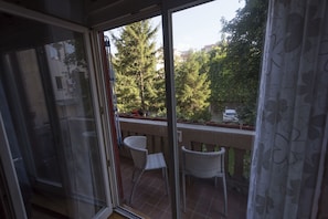 A balcony with two wicker chairs, a tiled floor, and a view of trees and a parked car.