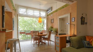 A cozy living room with a green sofa, wooden dining table, and chairs. There's a small stool and a radiator on the floor. - Apartments Harmony 18 (Belgrade)