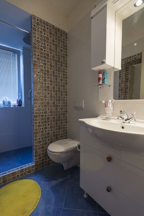 A bathroom with patterned tiles, a white sink, a mirror, and a yellow bath mat.