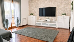A living room with a flat-screen TV mounted on a brick wall, wooden flooring, and a grey rug.