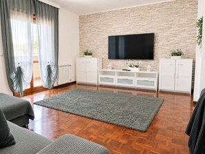 A living room with a flat-screen TV mounted on a brick wall, wooden flooring, and a grey rug.