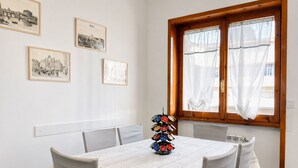 A dining area with a round table, white chairs, and a window with curtains.