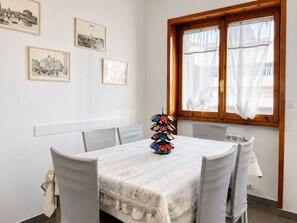 A dining area with a round table, white chairs, and a window with curtains.