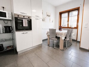 Una cocina moderna con armarios blancos, horno integrado, cafetera y comedor con mesa y sillas.