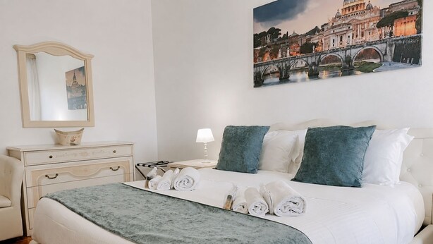A hotel room with a bed, a nightstand, a lamp, a mirror, and a painting of a cityscape.
