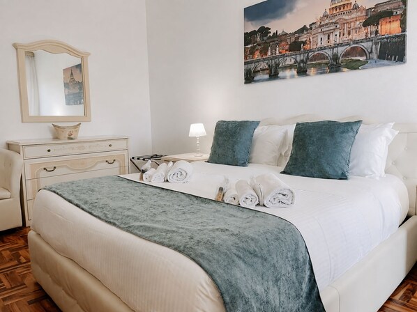 A hotel room with a bed, a nightstand, a lamp, a mirror, and a painting of a cityscape.