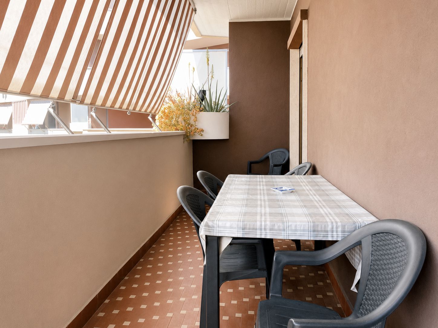 Un balcon avec une table et des chaises, un pot de fleurs et un auvent à rayures.