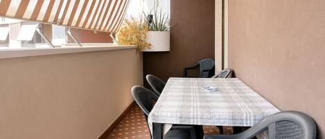 Un balcon avec une table et des chaises, un pot de fleurs et un auvent à rayures.