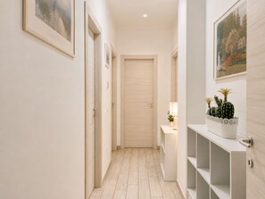 A hallway with a door at the end, a small table with a lamp, and a white console with decorative plants.