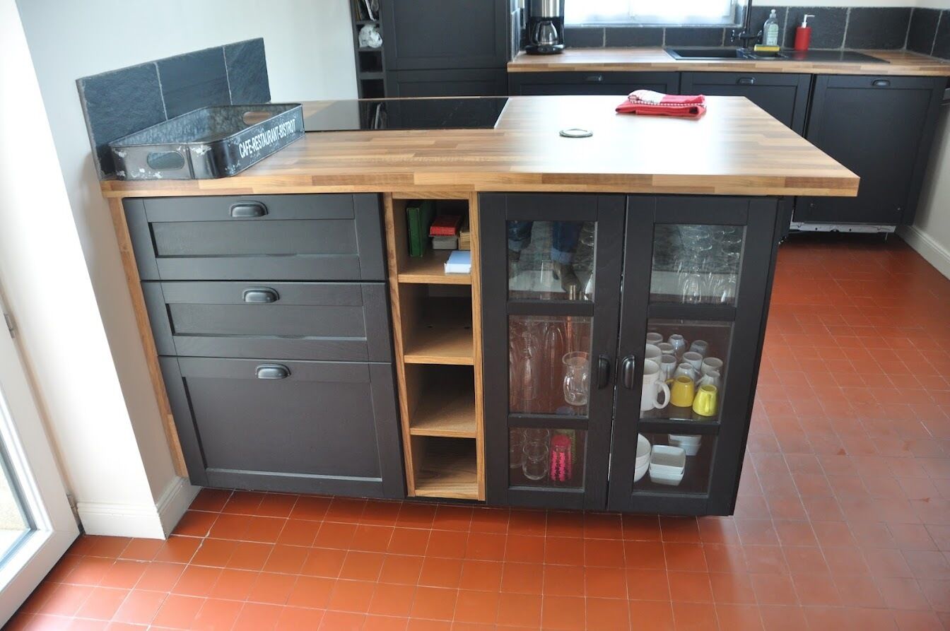 Une cuisine dotée d’un plan de travail en bois, de meubles de rangement gris et d’un meuble vitré contenant de la vaisselle et des verres.