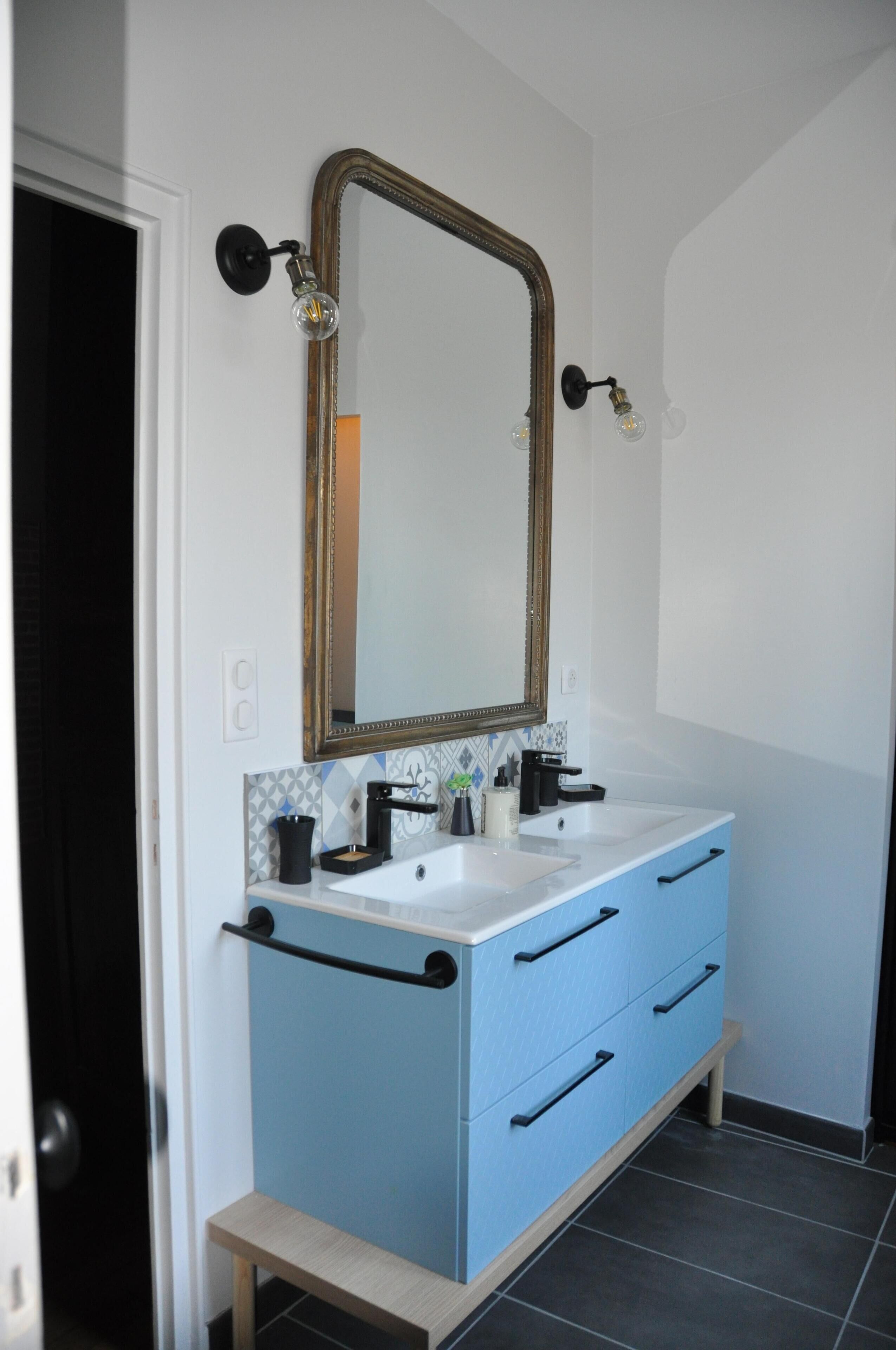 Un baño con lavamanos doble, un espejo con marco dorado y un mueble de tocador azul.