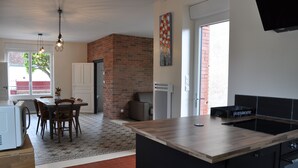 Una cocina moderna con una isla de madera, un comedor con mesa y sillas, y una pared de ladrillo.