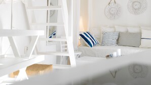 Dormitorio decorado en tonos blancos con cama, almohadas, una escalera y una cesta tejida.