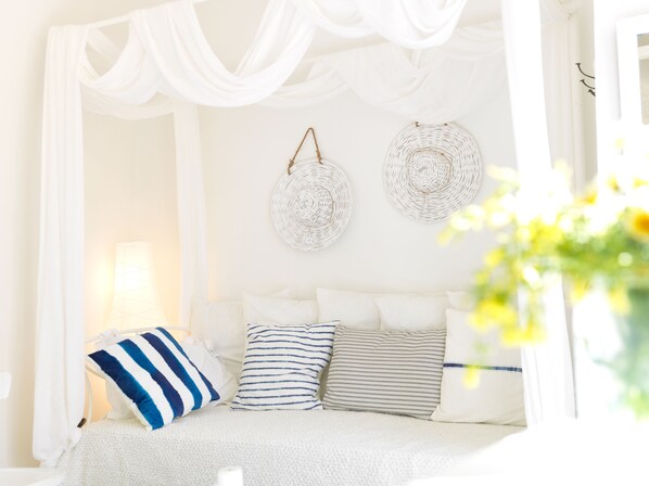 A bedroom with a canopy bed, white bedding, and two woven wall decorations. - Alsaki Suite Street View by K&K (Oia)